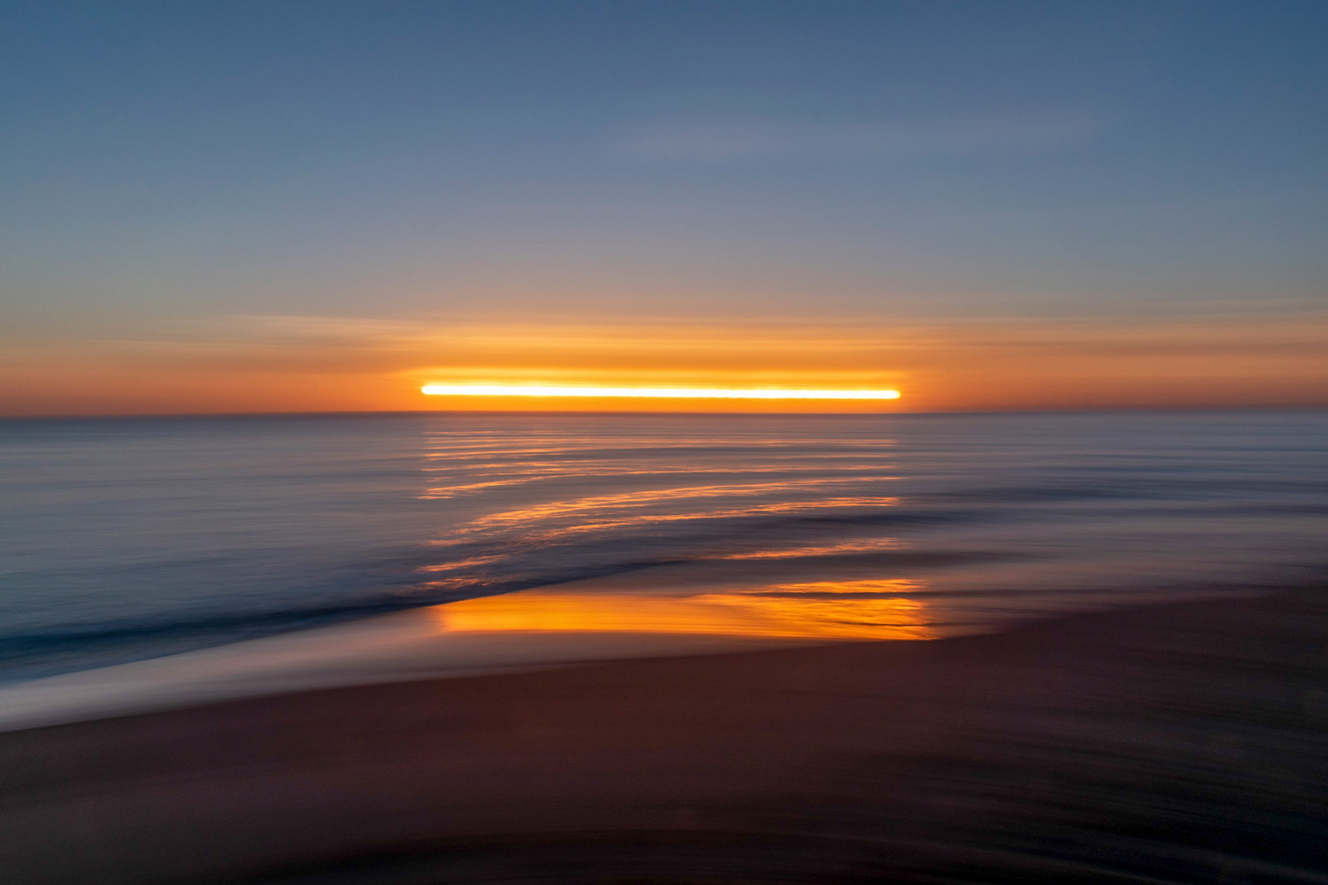 First light over open water, the sun a single line on the horizon.
